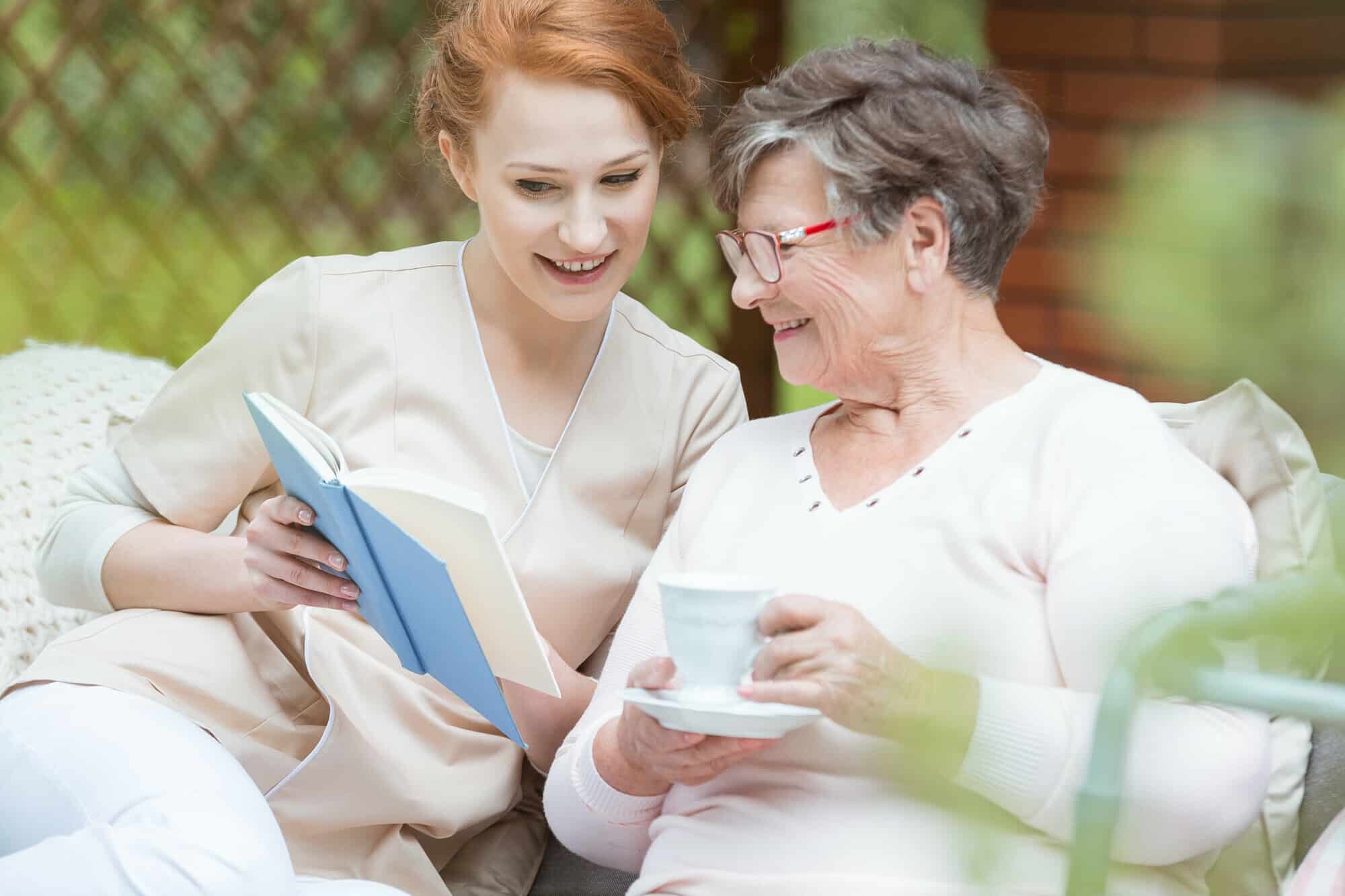 Caregiver and Senior citizen reading a book outside