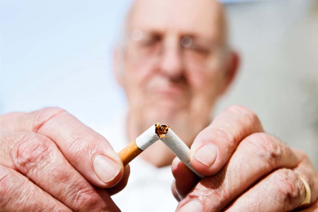 Senior man quitting smoking and breaking cigarette in half