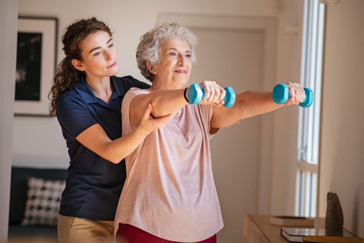 Caregiver helping a senior woman lift dumbbells